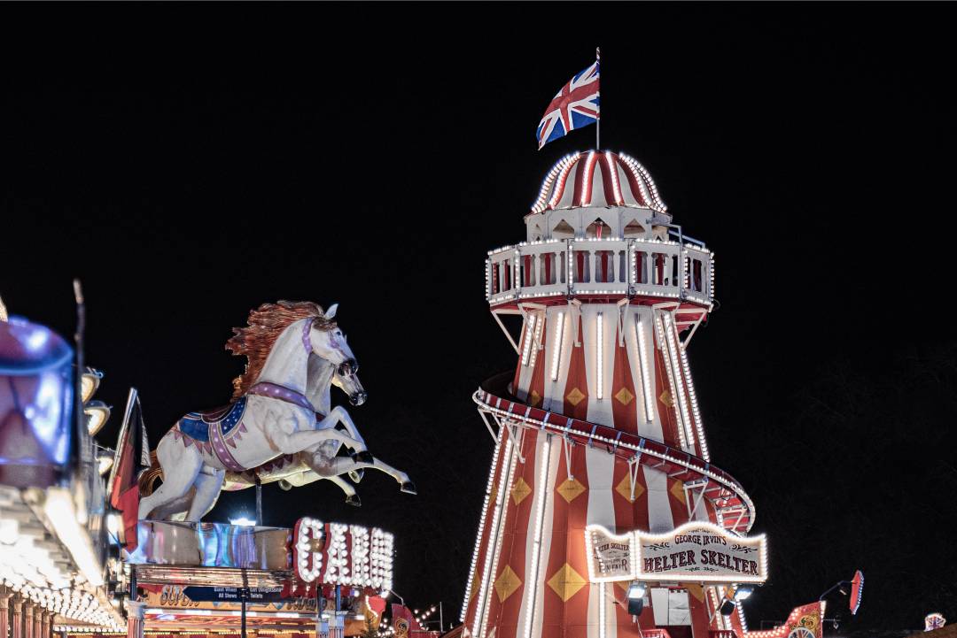 Picture of an amusement park at night with a Union Jack on top of a tower and a merry-go-round